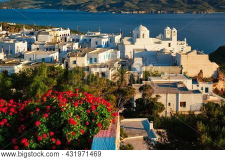 Picturesque scenic view of Greek town Plaka on Milos island over red geranium flowers and Orthodox greek church. Plaka village, Milos island, Greece