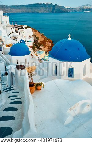 Famous view from viewpoint of Santorini Oia village with blue dome of whitewashed greek orthodox Christian church of traditional greek architecture. Oia town, Santorini island, Greece