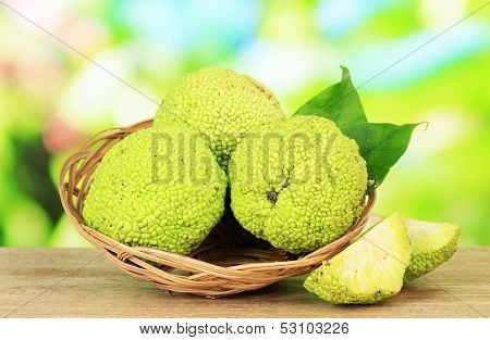 Osage Orange fruits (Maclura pomifera) in basket, on wooden table, on nature background