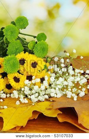 Beautiful flowers with yellow leaves on table on bright background