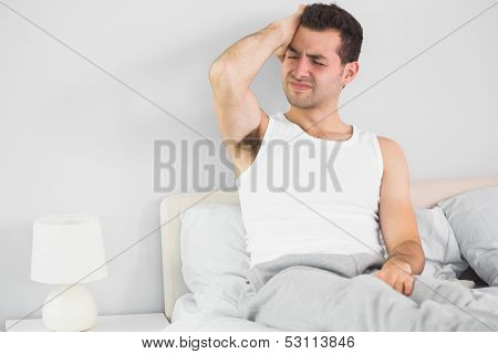 Wincing handsome man having a headache in bright bedroom