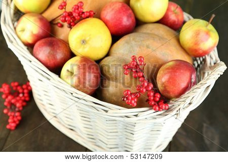 Juicy apples and pumpkin in wooden basket on table close-up