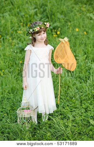 Little girl in white stands with butterfly net and coop on green meadow.