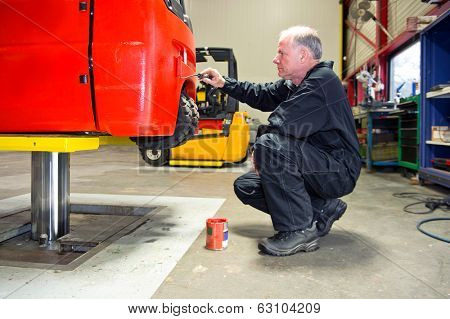 Mechanic repainting a forklift on a bridge in a workshop
