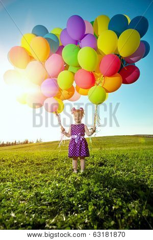 Happy little girl holding colorful balloons. Child playing on  green meadow. Smiling  kid. Portrait of baby outdoor 