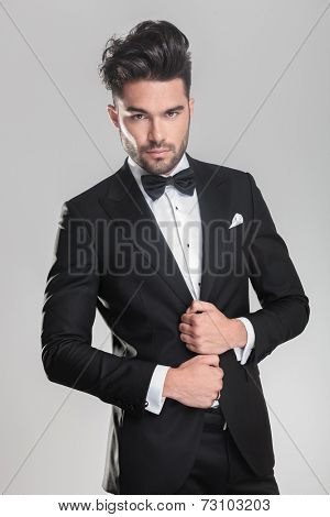 Close up of an elegant young man ajusting his tuxedo while looking at the camera