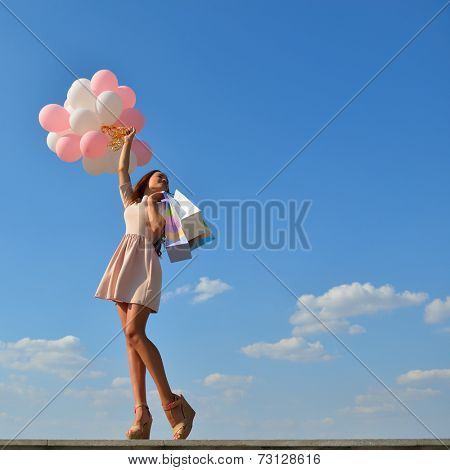 Beautiful girl holding shopping bags and colored balloons over blue sky