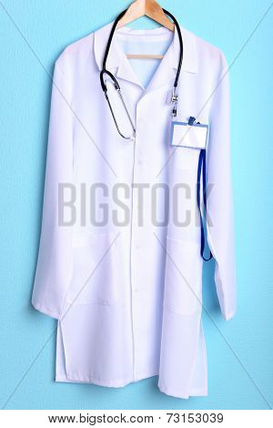 Doctor coat with stethoscope on hanger on blue background