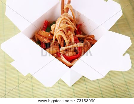 Fried noodles in takeaway box on mat background