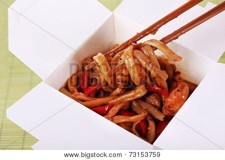 Fried noodles in takeaway box on mat background