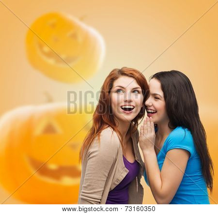 happiness, holidays, firendship and people concept - smiling teenage girls gossiping over halloween pumpkins background