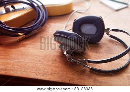 Music Recording scene. Professional grade headphones on a rustic or bare wooden table, with by-the-window type warm light. An electric guitar, memo pad , in the background. Shallow depth of field.