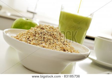 a bowl with oatmeal cereal, an apple and a glass with a green smoothie on the kitchen table