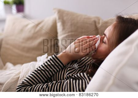 Portrait of a sick woman blowing her nose while sitting on the sofa