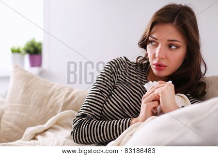 Portrait of a sick woman blowing her nose while sitting on the sofa