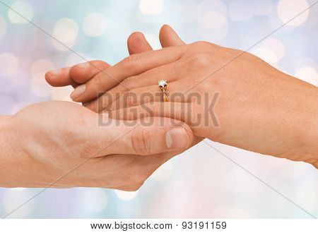 jewelry, couple, love and wedding concept - close up of man and woman hands with engagement ring over blue holidays lights background