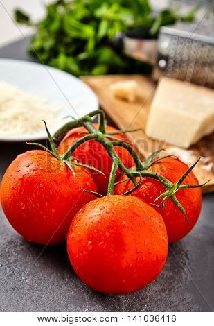 Branch of fresh red tomatoes with water drops on and parmesan or parmigiano reggiano cheese on back with grater and grated cheese on white plate and mint beam. Concept of italian cuisine ingredients