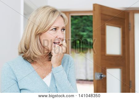 Sad Mature Woman Suffering From Agoraphobia Looking Out Of Open Door