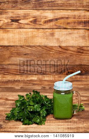 Jar tumbler mug with green smoothie drink and a bundle of fresh parsley on wooden table
