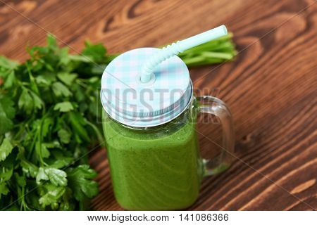 Jar tumbler mug with green smoothie drink and a bundle of fresh parsley on wooden table
