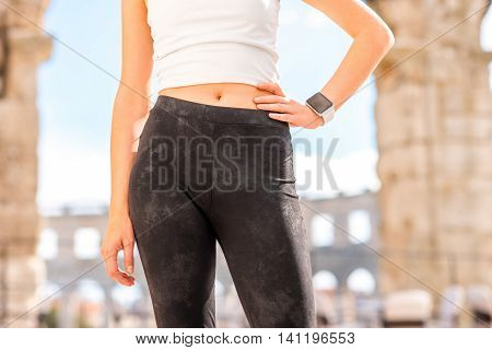 Beautiful waist of sports woman in white t-shirt and black leggings outdoors near the old roman amphitheatre