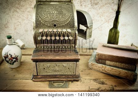 KOLMANSKOP NAMIBIA -JAN 27 2016: Vintage cash register on wooden table in retro style business office. Clay jug and cup out-of-print books and glass bottle with dried flowers. All covered a dust. Filtered image