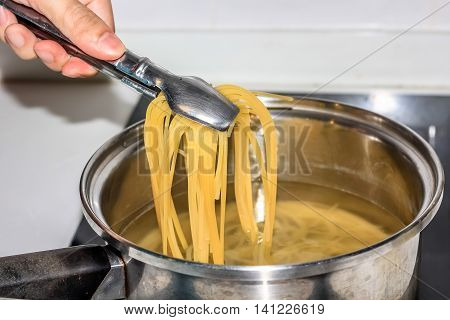 people use tong to pick boiling spaghetti noodles in the pot