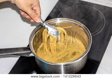 people use tong to pick boiling spaghetti noodles in the pot