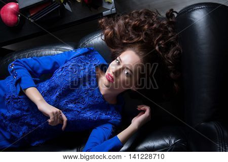 Young beautiful brunette girl lies on a leather couch and stares into the camera. Shooting from above.