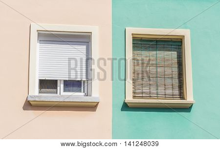 two windows with colorful facade of a residential building wooden shutters orange and green pastel