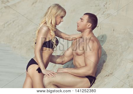 Man and woman passionately look into each other's eyes they are on the sandy beach.