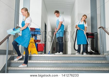 Group Of Happy Male And Female Janitor Cleaning Corridor With Cleaning Equipments