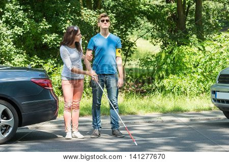 Young Woman Helping Blind Man Wearing Armband On Street