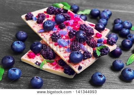 Large chocolate bars white blackberries blueberries blueberry raspberry candied violet petals mint leaves candy heart on a dark black background wooden surface