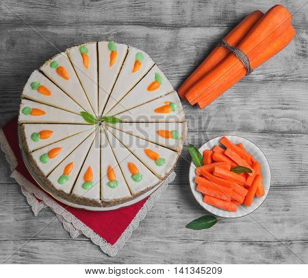 Carrot cake sprinkled with nuts decorated with cream-colored carrots on stand for cakes fresh whole carrots sliced sticks carrots on light white background wooden top view