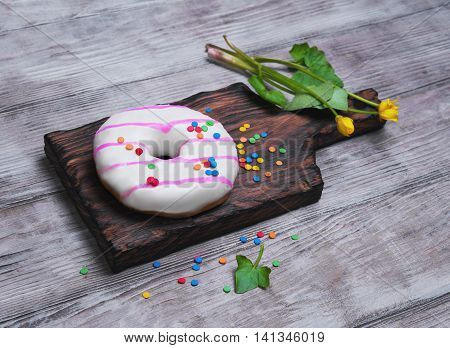Donut with white and pink icing sprinkled sprinkling colored for donuts yellow flowers on light wooden background