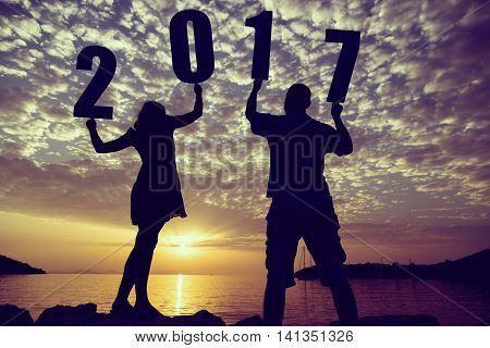 Silhouette of a couple in love standing on a rocky shore holding numbers 2017 and looking at a beautiful sunset at Syvota bay Greece