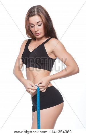 Slender girl with a sports figure measures the waist. Brunette in black lingerie. Isolated.