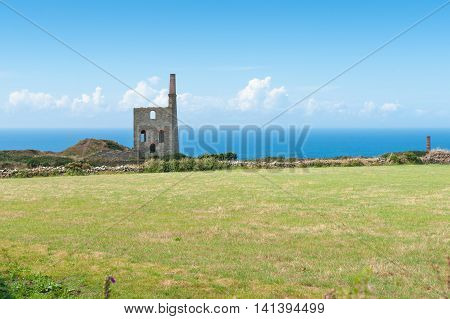 Remains of historic tin mine stone engine house across green field on coast of Cornwall England