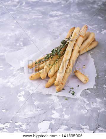 Fresh homemade crispy bread sticks with thyme and sea salt on a gray concrete background with fresh herbs. selective focus