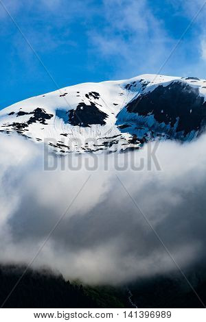  Closeup of one of the many mountain peaks seen while cruising the Tracy Arm Fjord in Alaska. Blue sky low clouds crisp snow and ice reflections of the Tongass National Forest.
