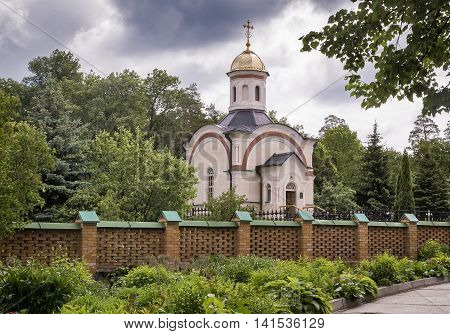 A beautiful Orthodox temple located on a hill surrounded by flowers and plants: arborvitae blue spruce shrubs.