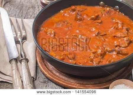 Beef stew with tomato sauce in a pan on wooden background