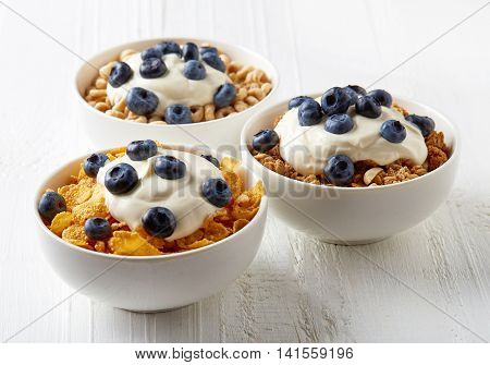 Three Types Of Cereals With Yogurt And Blueberries On White Table