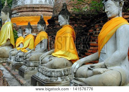 Ayutthaya Thailand - December 28 2005: A row of seated Buddhas draped with orange and saffron silk sashes at Wat Yai Chai Mongkon