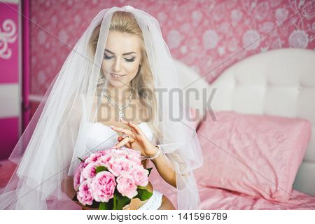 Beautiful sexy young women underwear sitting on a bed with a bouquet of flowers in hands and with a veil on her head. Last preparations for the wedding. Morning the bride.