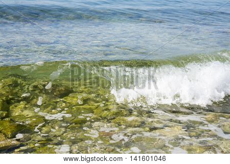 Sea wave covers stones with foam on pebble beach