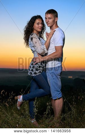 romantic couple embrace at sunset, beautiful landscape and bright yellow sky, love tenderness concept, young adult people