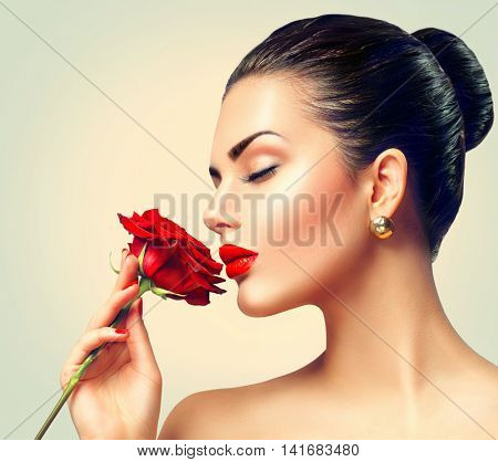 Beauty Woman with red rose. Fashion Brunette Model Girl face Portrait with Red Rose in her hand. Red Lips and Nails. Beautiful Luxury Makeup and Manicure. Vogue Style