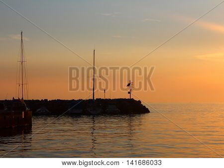 A pier with yachts nearby at a orange sunset on the Mediterranean